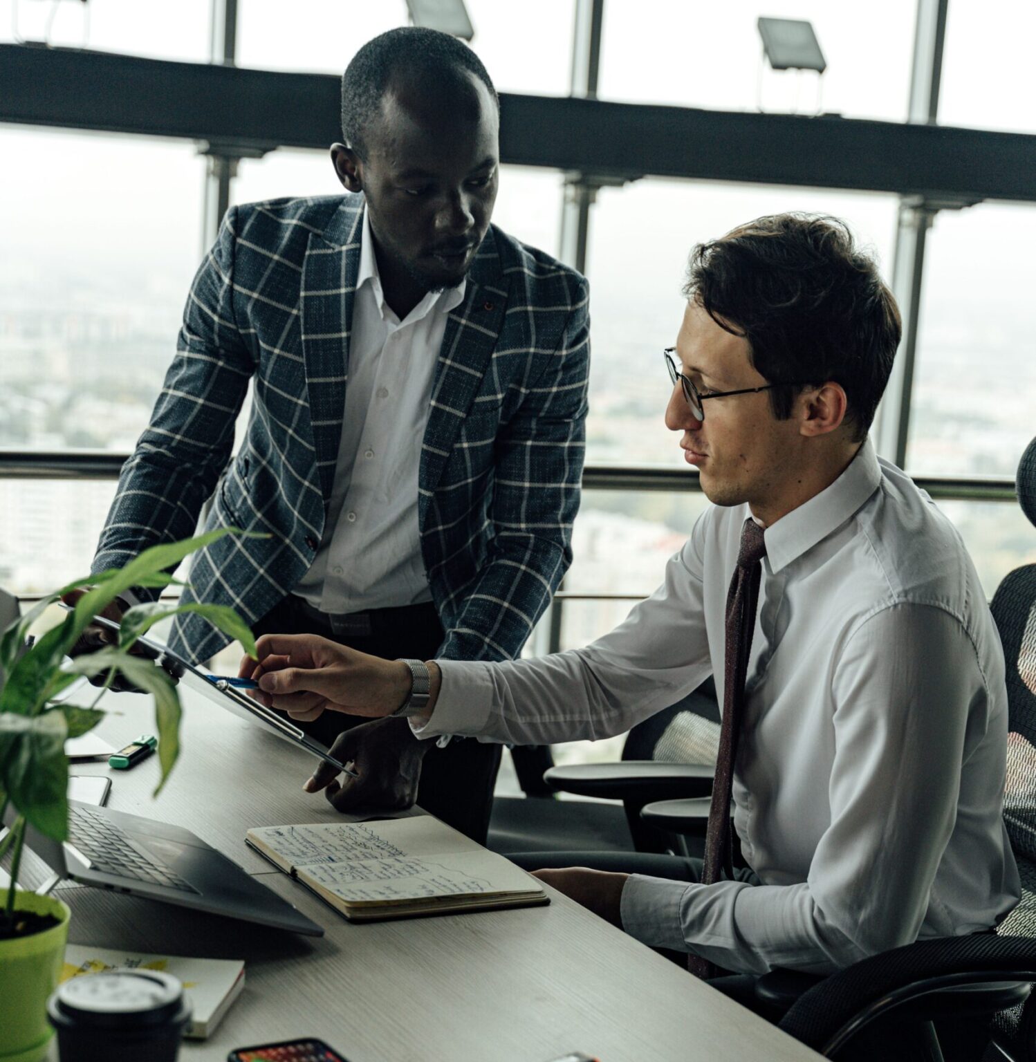 Two businessmen discussing projects in a modern high-rise office setting.