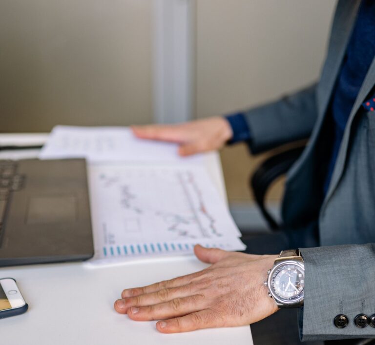 Businessman analyzing charts and graphs at his desk with a laptop and smartphone.